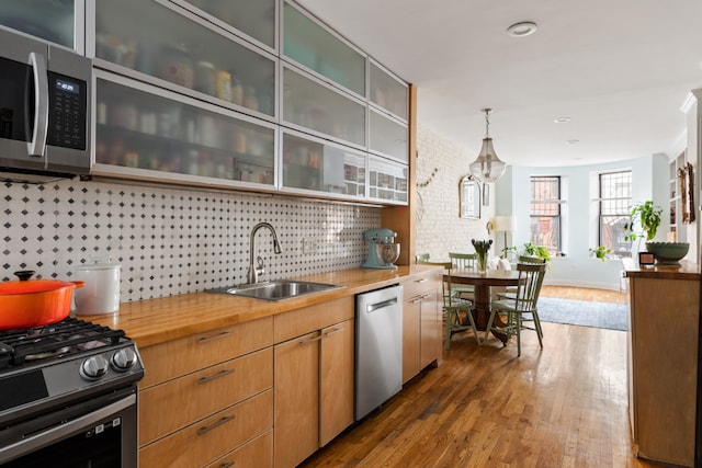 kitchen featuring butcher block countertops, stainless steel appliances, backsplash, hanging light fixtures, and sink