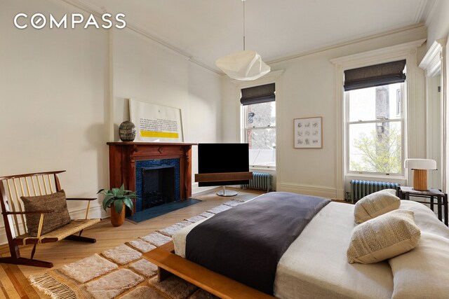 bedroom featuring radiator, wood-type flooring, multiple windows, and ornamental molding