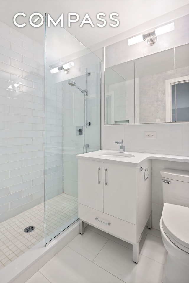 bathroom featuring tile patterned flooring, toilet, vanity, and tiled shower