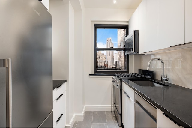 kitchen with appliances with stainless steel finishes, white cabinets, baseboards, a sink, and backsplash