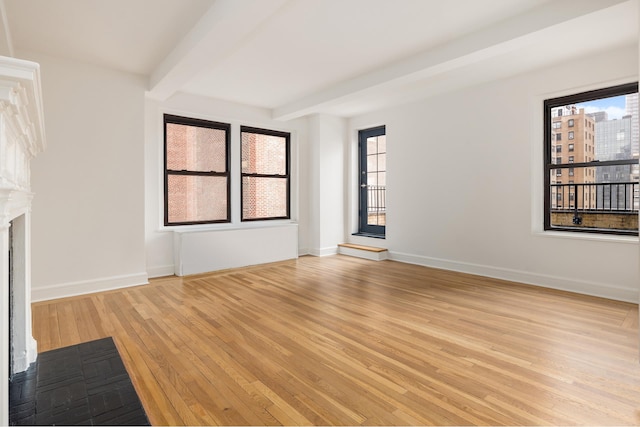 unfurnished living room featuring hardwood / wood-style flooring, beamed ceiling, healthy amount of natural light, and baseboards