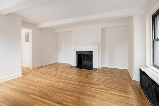 unfurnished living room with radiator, a fireplace, light wood-style floors, plenty of natural light, and beamed ceiling