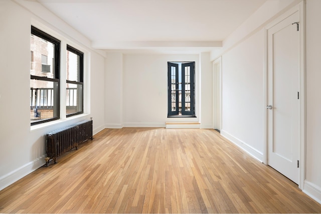 spare room with radiator heating unit, light wood-style floors, and baseboards