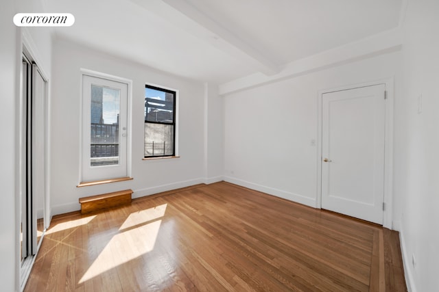 empty room with light wood-type flooring and beamed ceiling