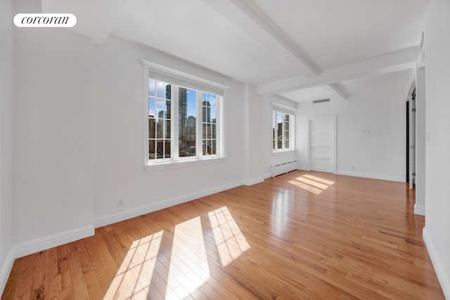 unfurnished living room with a baseboard heating unit, beam ceiling, and light wood-type flooring