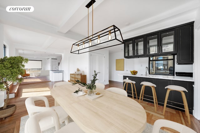 dining room featuring beam ceiling, light hardwood / wood-style flooring, and sink