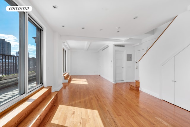 unfurnished living room with electric panel, light hardwood / wood-style floors, and beamed ceiling