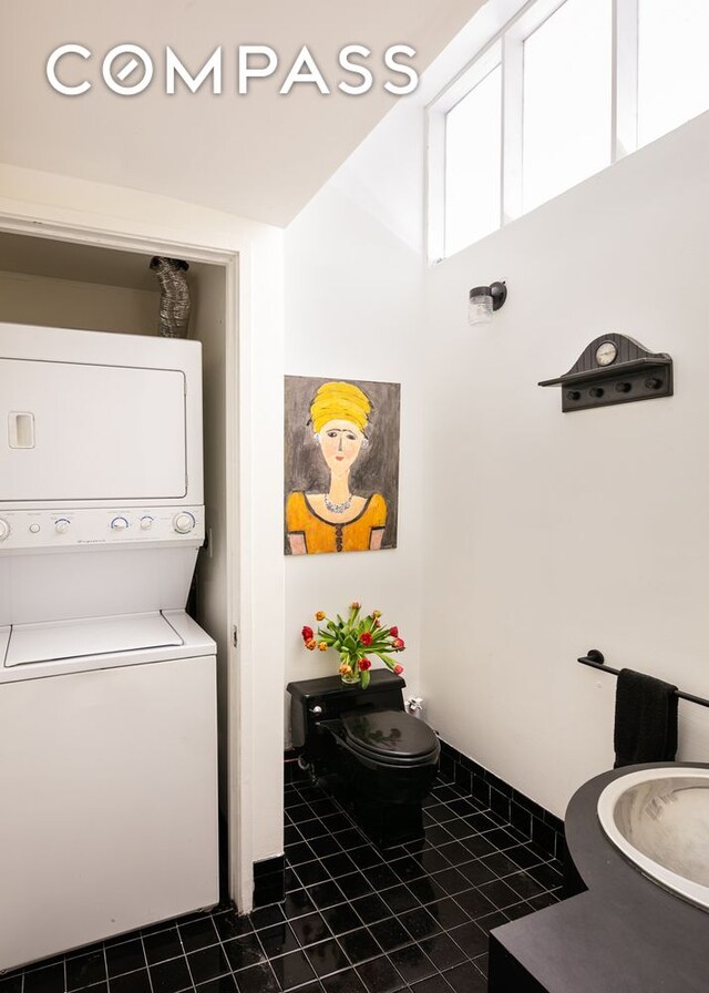 clothes washing area featuring stacked washer and dryer and dark tile patterned flooring