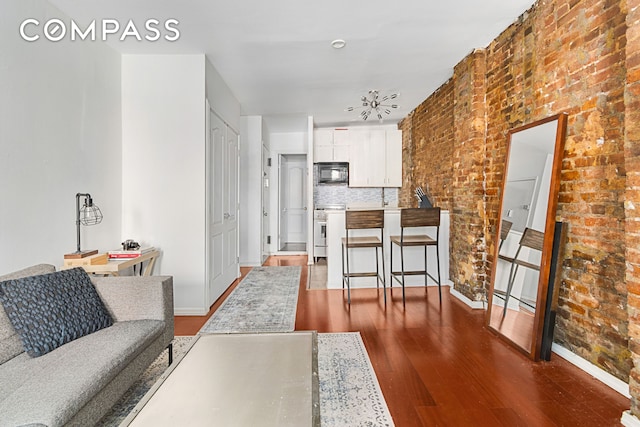 living area featuring baseboards, brick wall, and wood finished floors