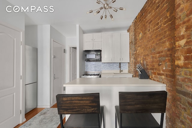 kitchen featuring gas range, black microwave, light countertops, white cabinets, and an inviting chandelier