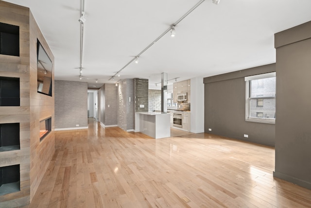 unfurnished living room featuring a large fireplace, rail lighting, baseboards, and light wood finished floors