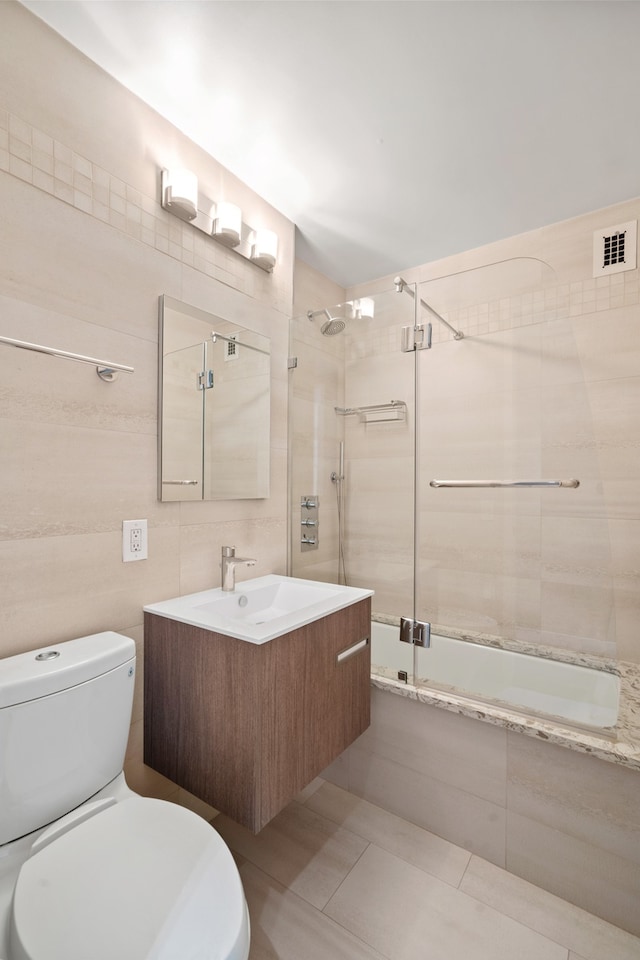 bathroom featuring visible vents, toilet, tiled shower / bath combo, vanity, and tile walls