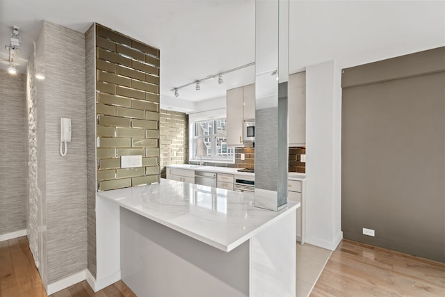 kitchen featuring appliances with stainless steel finishes, light wood-style flooring, a sink, a peninsula, and rail lighting