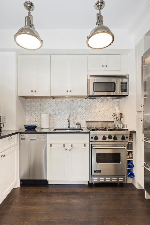 kitchen featuring a sink, high quality appliances, dark countertops, and white cabinetry