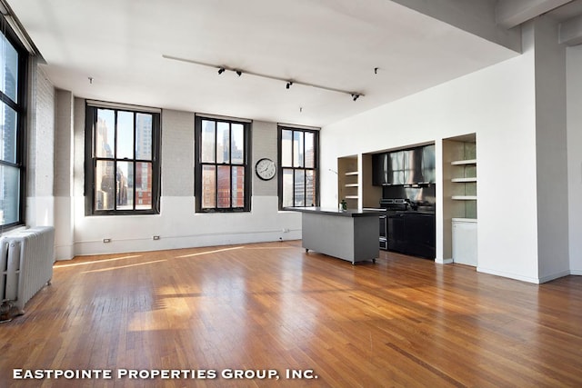 unfurnished living room featuring wood-type flooring, radiator, and track lighting