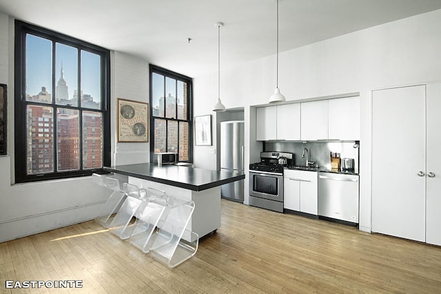 kitchen featuring stainless steel appliances, dark countertops, a sink, and light wood-style flooring