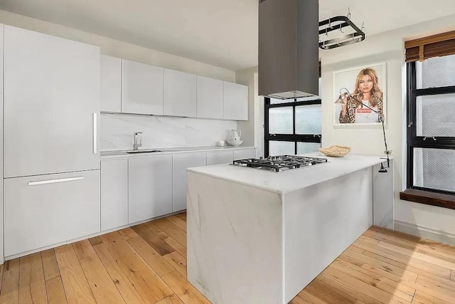 kitchen with sink, white cabinets, island exhaust hood, stainless steel gas cooktop, and light wood-type flooring