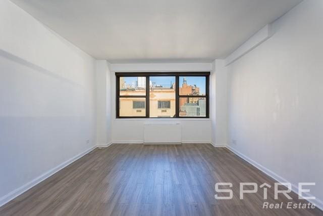 unfurnished room with radiator heating unit, baseboards, and dark wood finished floors