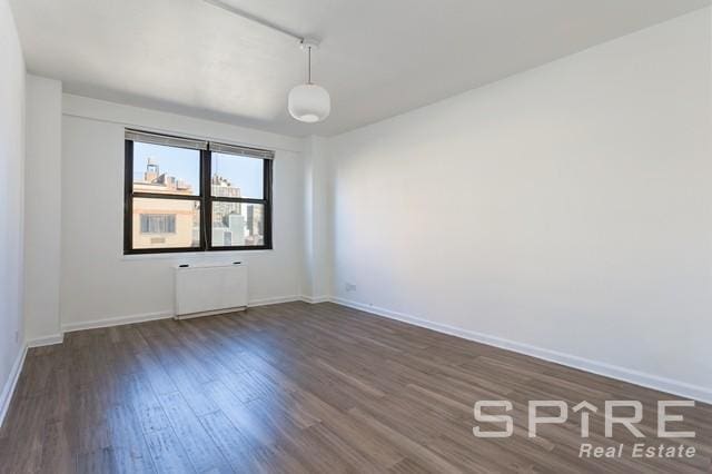empty room featuring radiator heating unit, baseboards, and dark wood-style floors