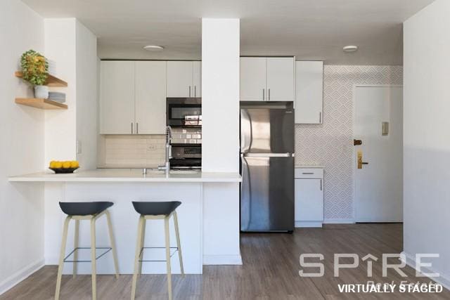 kitchen with white cabinets, a peninsula, freestanding refrigerator, and a kitchen breakfast bar