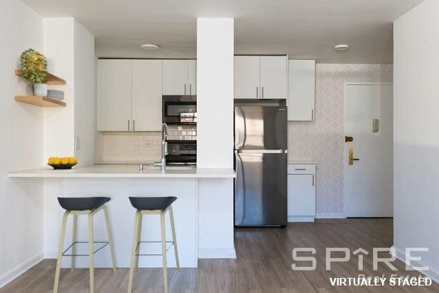 kitchen with white cabinets, freestanding refrigerator, a breakfast bar, and dark wood-style floors