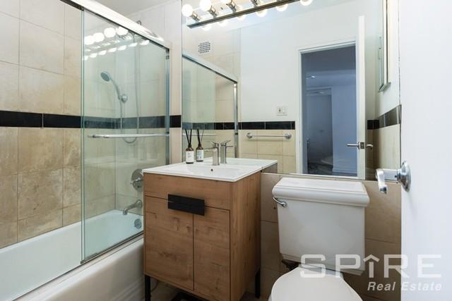 bathroom with toilet, enclosed tub / shower combo, tile walls, and vanity