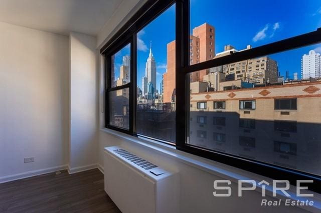 interior details with radiator heating unit, baseboards, a city view, and wood finished floors