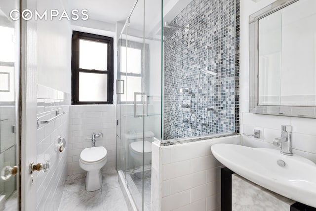 bathroom featuring tile walls, toilet, a stall shower, and a sink