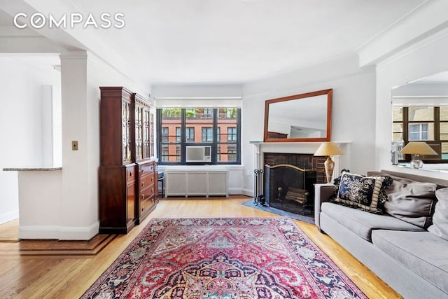 living room featuring light wood-style floors, baseboards, a fireplace with flush hearth, and radiator heating unit