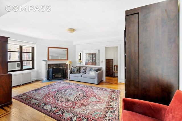 bedroom with cooling unit, a brick fireplace, and wood finished floors