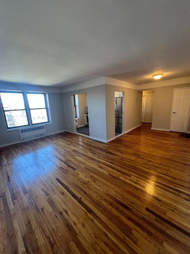 unfurnished living room with radiator heating unit, dark wood-type flooring, and baseboards