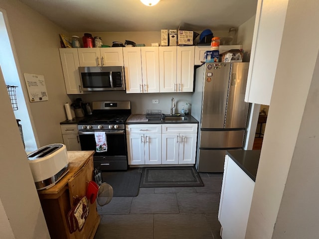 kitchen with a sink, stainless steel appliances, dark countertops, and dark tile patterned floors