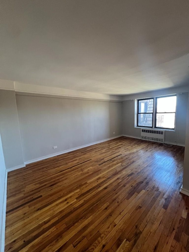 unfurnished room with dark wood finished floors, an AC wall unit, and baseboards