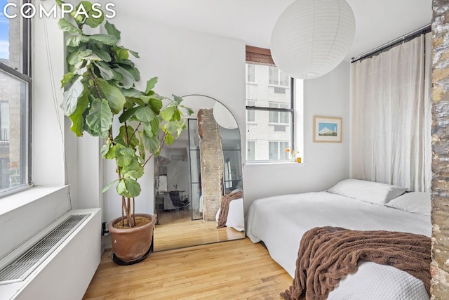 bedroom featuring a wall unit AC, hardwood / wood-style flooring, and multiple windows