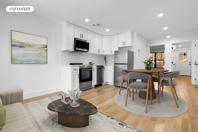 kitchen with stainless steel appliances, light wood-style floors, visible vents, and decorative backsplash