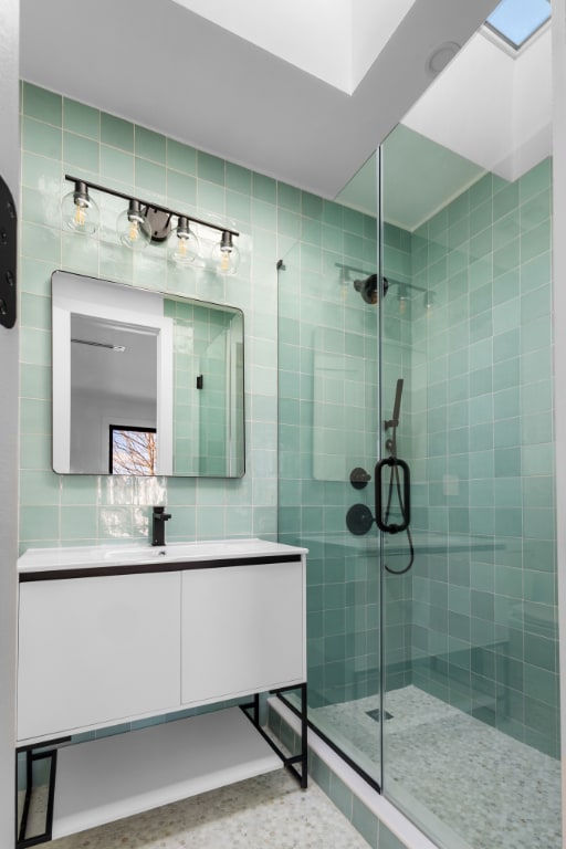 bathroom featuring a stall shower, vanity, tile walls, and a skylight