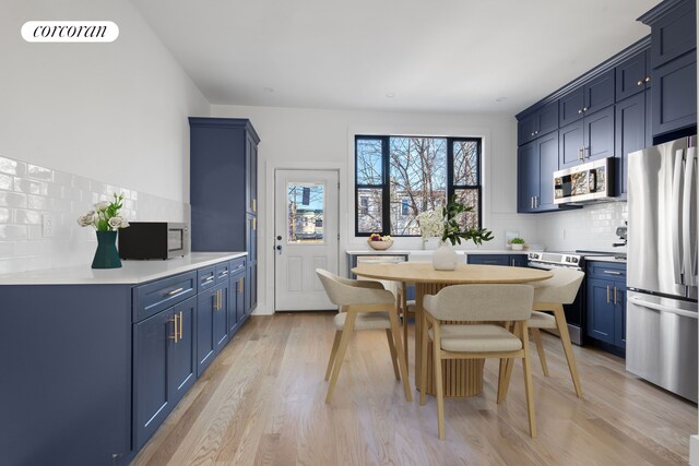 kitchen featuring backsplash, light hardwood / wood-style flooring, blue cabinetry, and appliances with stainless steel finishes