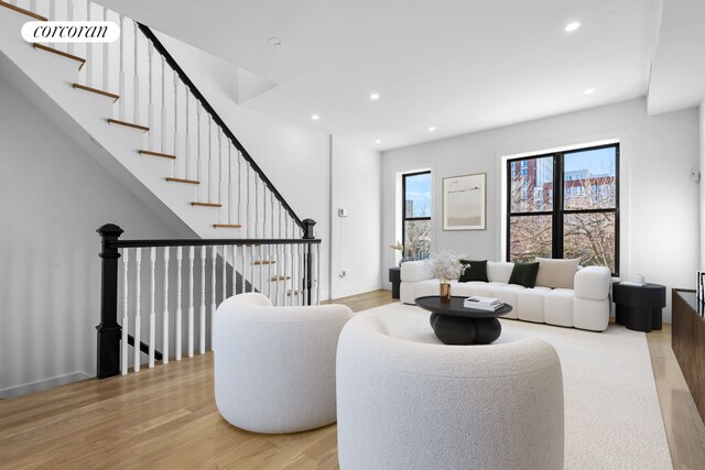 living room featuring baseboards, light wood finished floors, stairs, and recessed lighting