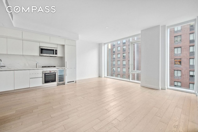 unfurnished living room featuring floor to ceiling windows, sink, wine cooler, and light wood-type flooring