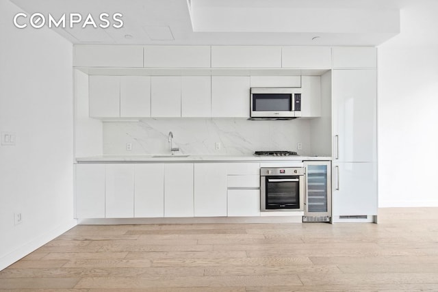 kitchen featuring sink, appliances with stainless steel finishes, white cabinetry, wine cooler, and light hardwood / wood-style floors