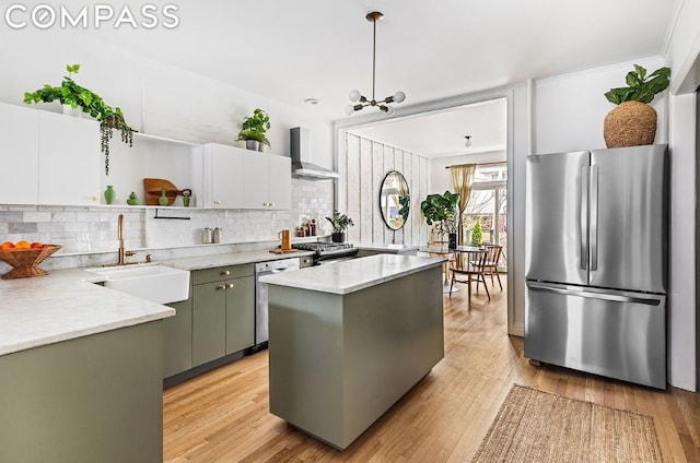 kitchen with a center island, sink, hanging light fixtures, stainless steel appliances, and wall chimney exhaust hood