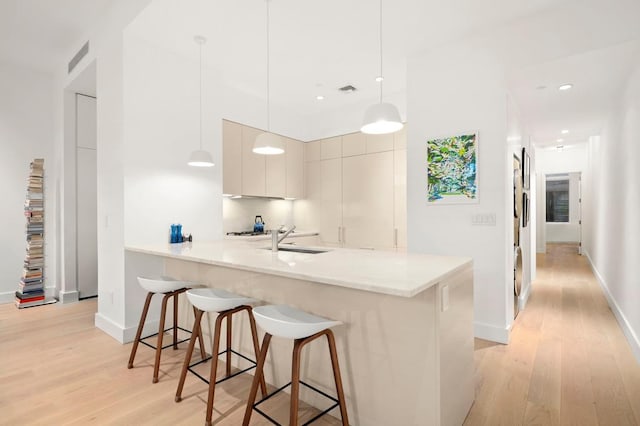 kitchen featuring a sink, light wood finished floors, modern cabinets, a kitchen bar, and a peninsula