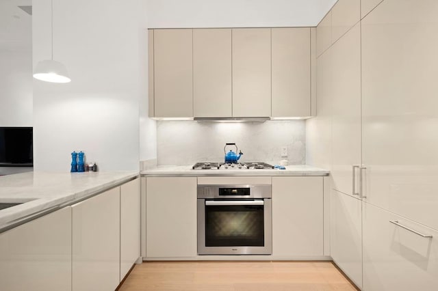 kitchen with stainless steel appliances, modern cabinets, light wood-type flooring, under cabinet range hood, and decorative light fixtures