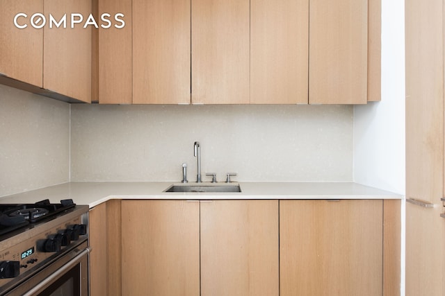 kitchen with light brown cabinets, stainless steel stove, backsplash, and a sink