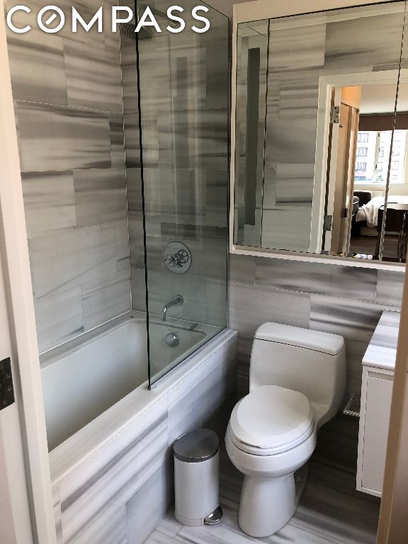 bathroom featuring toilet, tiled shower / bath, and tile walls