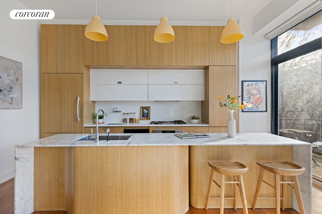 kitchen with decorative light fixtures, white cabinetry, sink, a kitchen breakfast bar, and light stone countertops