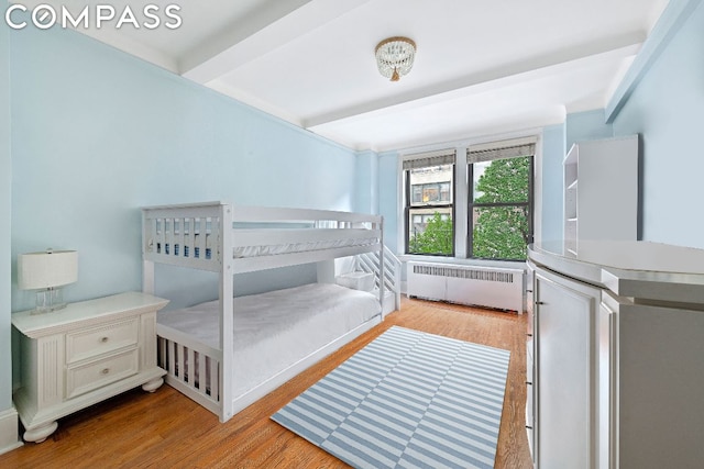 bedroom with radiator heating unit, beam ceiling, and light hardwood / wood-style floors