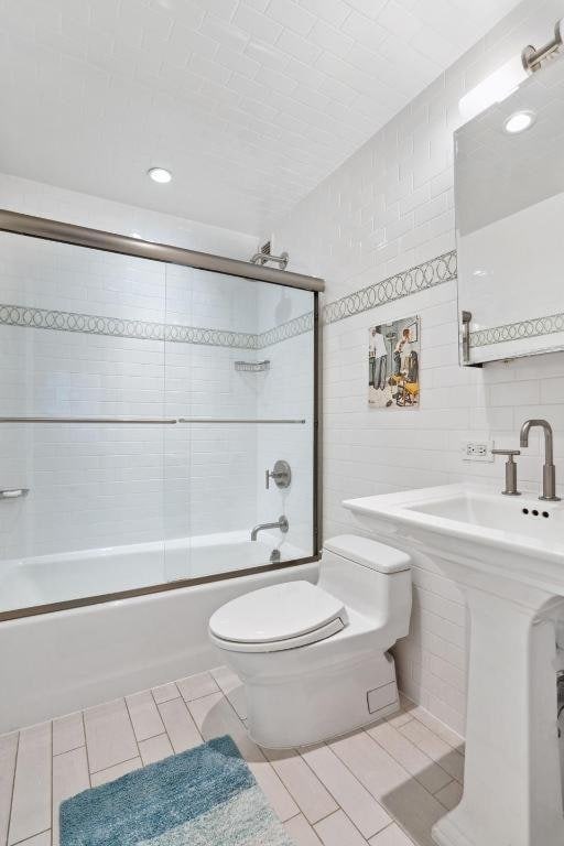 bathroom featuring enclosed tub / shower combo, tile walls, tile patterned floors, and toilet