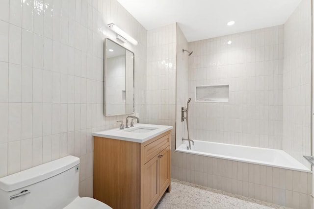 full bath featuring tile walls, tiled shower / bath, toilet, vanity, and speckled floor