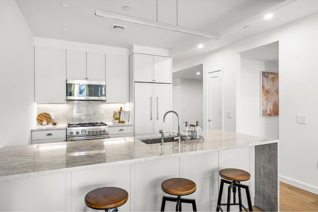 kitchen with premium appliances, decorative backsplash, white cabinetry, light stone countertops, and a kitchen bar